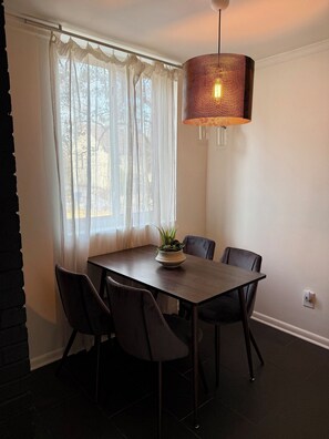 Un espace repas comprenant une table, des chaises, un luminaire suspendu et une fenêtre ornée de rideaux légers.