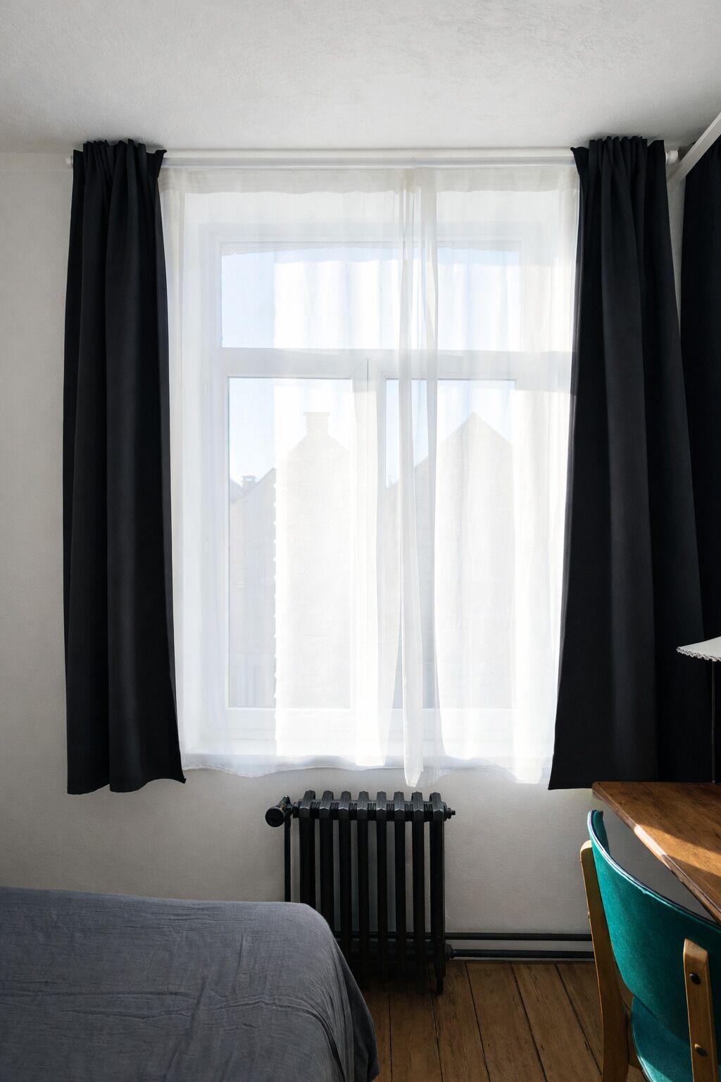 Een kamer met een groot raam, een radiator, een bed en een tafel.