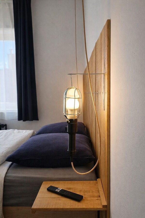 A hotel room with a bed, a bedside table with a remote control, and a wall-mounted lamp. - La Maison Fives (Lille)