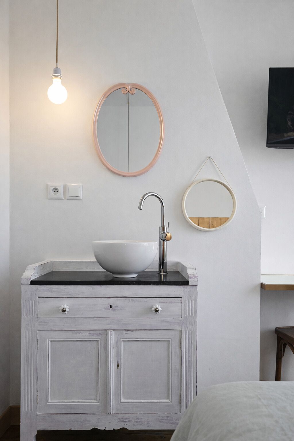 Een badkamer met een wit wastafel, een ronde spiegel en een lamp.