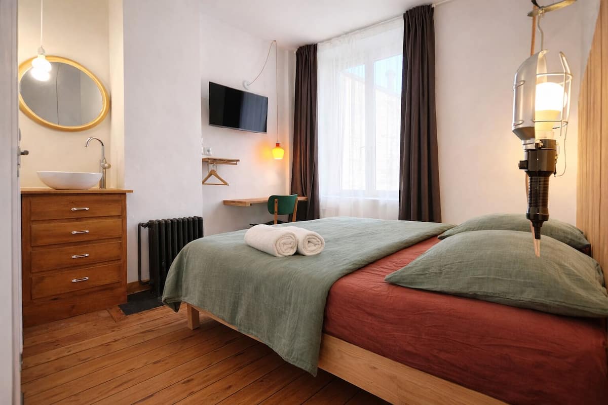 A bedroom with a bed, a dresser, a TV, a radiator, and a window with curtains.