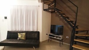 Una sala de estar con un sofá negro, un televisor y una escalera de madera.