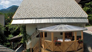 Een chalet met een schuin dak, een overdekte veranda met houten leuningen, en een kleine bloementuin.