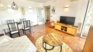 Ein Wohnzimmer mit einer Couch, einem Esstisch mit Stühlen, einem Fernseher auf einem Holzschrank und einem Teppich mit Muster.