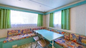 A compact room with a bench and a table, large windows with green curtains, and a geometric patterned floor. - Mobile home with terrace - 6 guests (Montblanc)