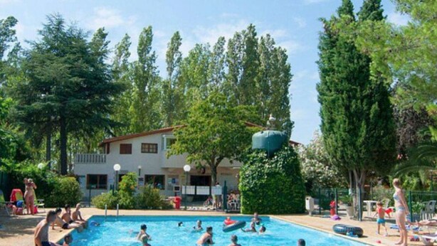 A swimming pool with people enjoying the water, surrounded by trees and a building with a red roof. - Mobile home with terrace - 6 guests (Montblanc)