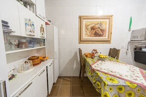 Une cuisine compacte avec des meubles blancs, un réfrigérateur et une table à manger agrémentée d’une nappe à motifs de tournesols.