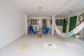 Une pièce avec un sol carrelé, une table à manger entourée de chaises bleues, un hamac et une porte verte.