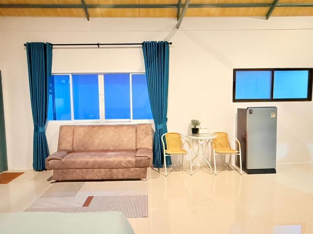 A room with a sofa, two chairs, a small table, a refrigerator, and a window with curtains.