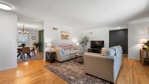Una sala de estar moderna con un sofá, un televisor y una zona de comedor con sillas y una mesa.