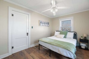 Ein Schlafzimmer mit Bett, Deckenventilator, Fenster mit Jalousien, Nachttisch und Tür.