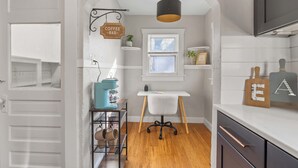 A kitchen with a coffee bar, a window with blinds, a hanging sign, and a shelf with a plant.