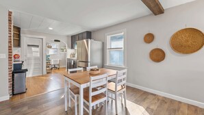 A modern kitchen with white cabinets, a stainless steel refrigerator, and a wooden dining table with white chairs.