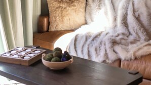 Un salon chaleureux avec un canapé en cuir marron, un plaid en fausse fourrure blanche et une table basse en bois sur laquelle se trouve un bol rempli de collations.