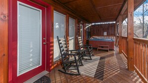 Een houten terras met schommelstoelen, een jacuzzi en een rode deur.