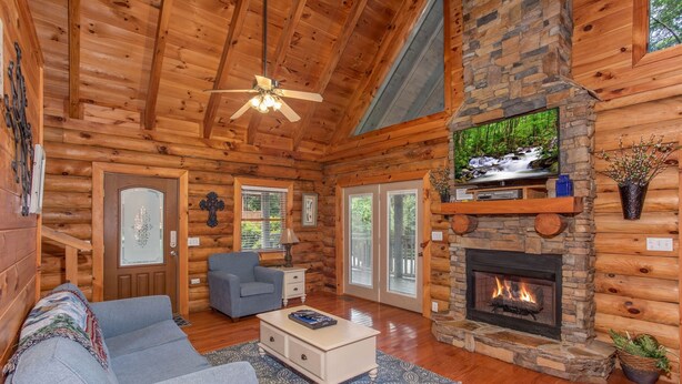 A log cabin interior with a stone fireplace, a television mounted above it, and a cozy seating area with a sofa and a coffee table. - Resort Setting*Close to Pigeon Forge*Romantic (PIGEON FORGE)