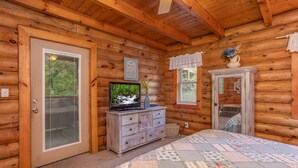 A log cabin bedroom with a wooden ceiling, a television on a dresser, a quilt on the bed, and a window with lace curtains. - Resort Setting*Close to Pigeon Forge*Romantic (PIGEON FORGE)