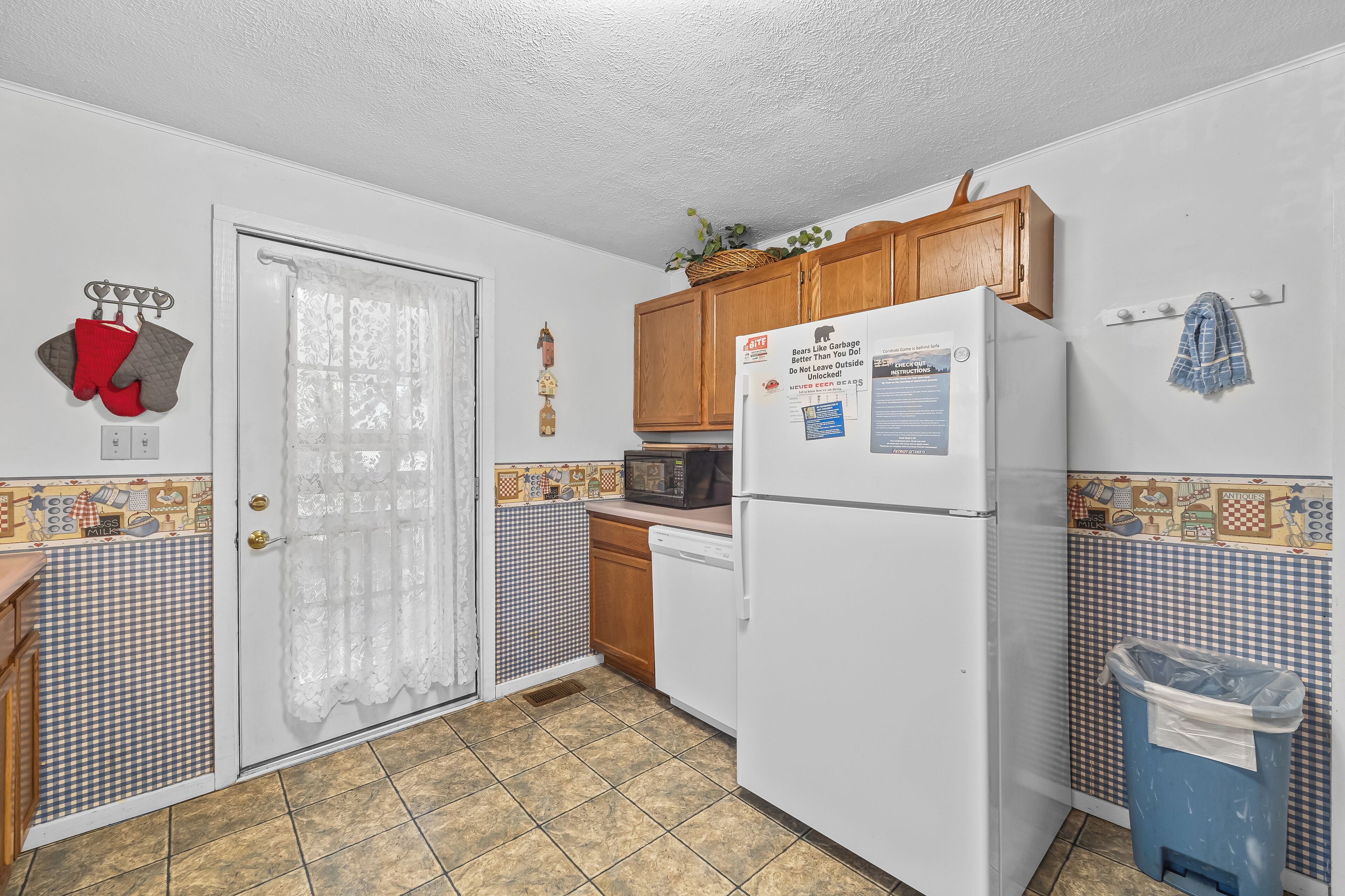 A kitchen with a refrigerator, microwave, wooden cabinets, and a trash bin.