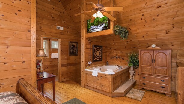 L’intérieur d’un chalet en bois comprend un lit en bois, une salle de bain avec baignoire, un ventilateur de plafond et un meuble en bois.