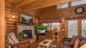 L’intérieur d’un chalet confortable, avec une cheminée en pierre, des meubles en bois et un téléviseur.