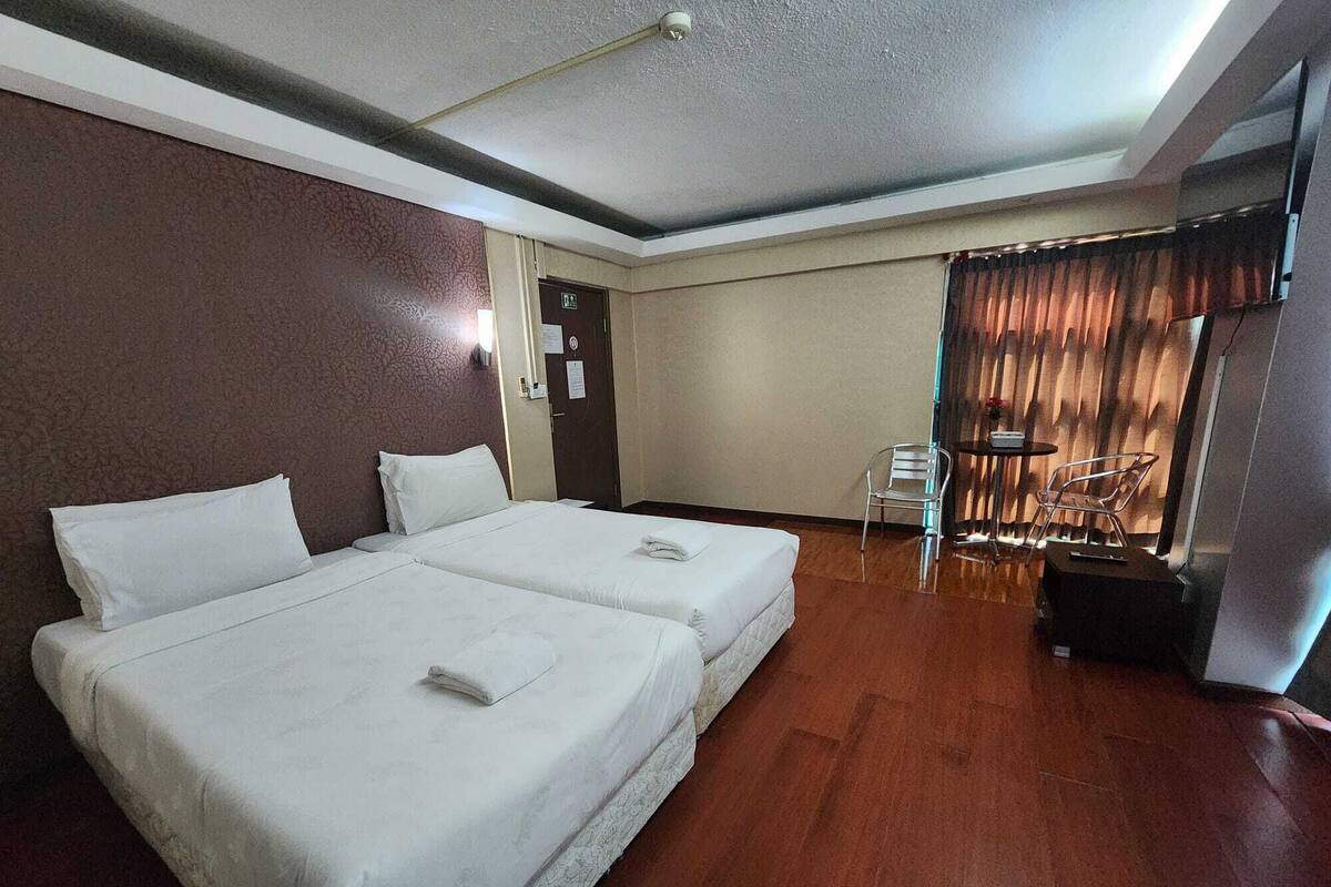 A hotel room with two beds, a small table, a chair, and a curtain.