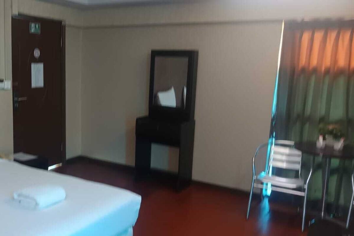 A hotel room with a bed, a desk, a chair, a mirror, and a window with curtains.
