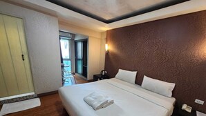 A hotel room with a large bed, a bedside table with a phone, and a view of the balcony. - New VC Hotel Bangkok (Bangkok)