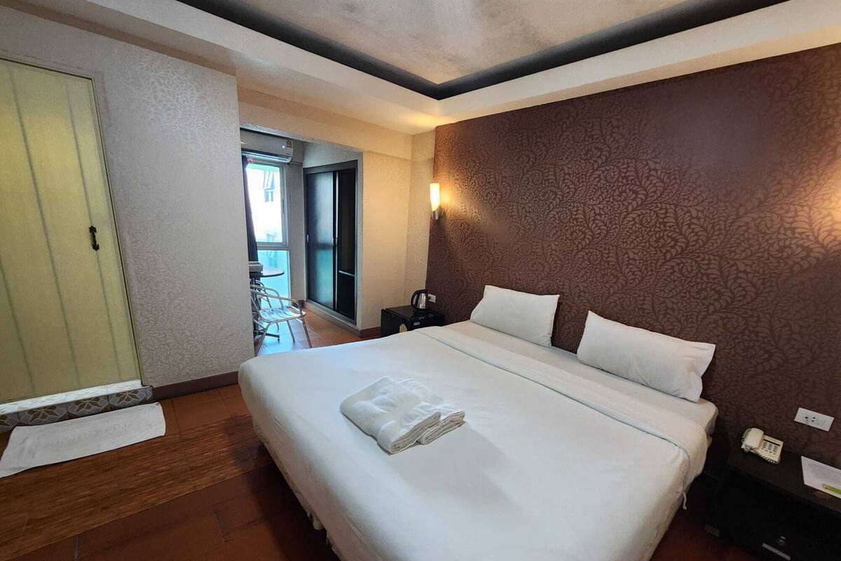 A hotel room with a large bed, a bedside table with a phone, and a view of the balcony.
