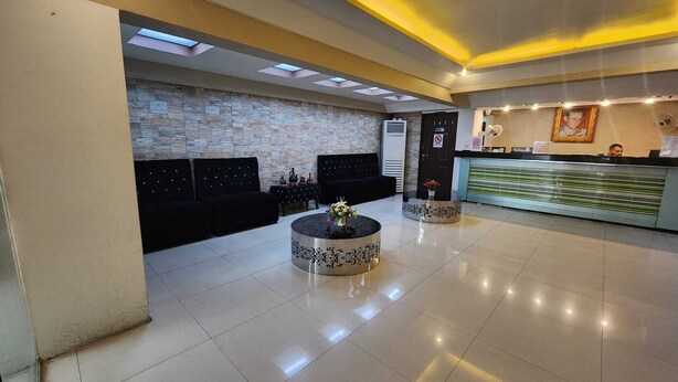 A hotel lobby with a reception desk, black sofas, a stone wall, and a tiled floor. - New VC Hotel Bangkok (Bangkok)