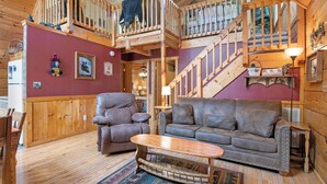 A cozy cabin interior with a wooden staircase, a leather sofa, a cushioned armchair, and a wooden coffee table. - Caught Up In The Mountains (PIGEON FORGE)