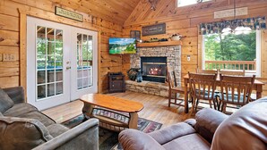 A cabin interior with a stone fireplace, wooden furniture, and a television mounted above it. - Caught Up In The Mountains (PIGEON FORGE)