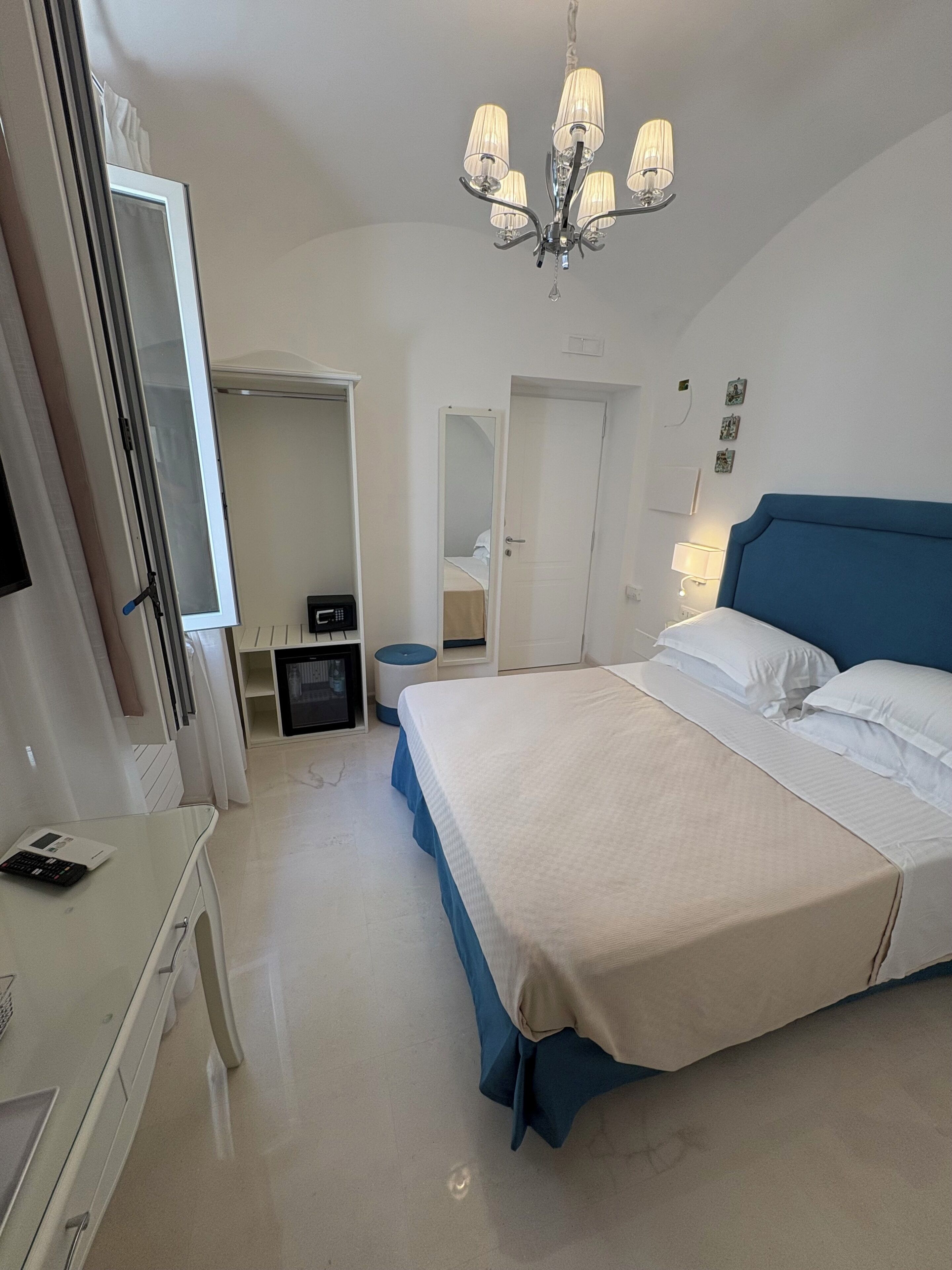 A hotel room with a large bed, a desk, a mirror, and a chandelier.
