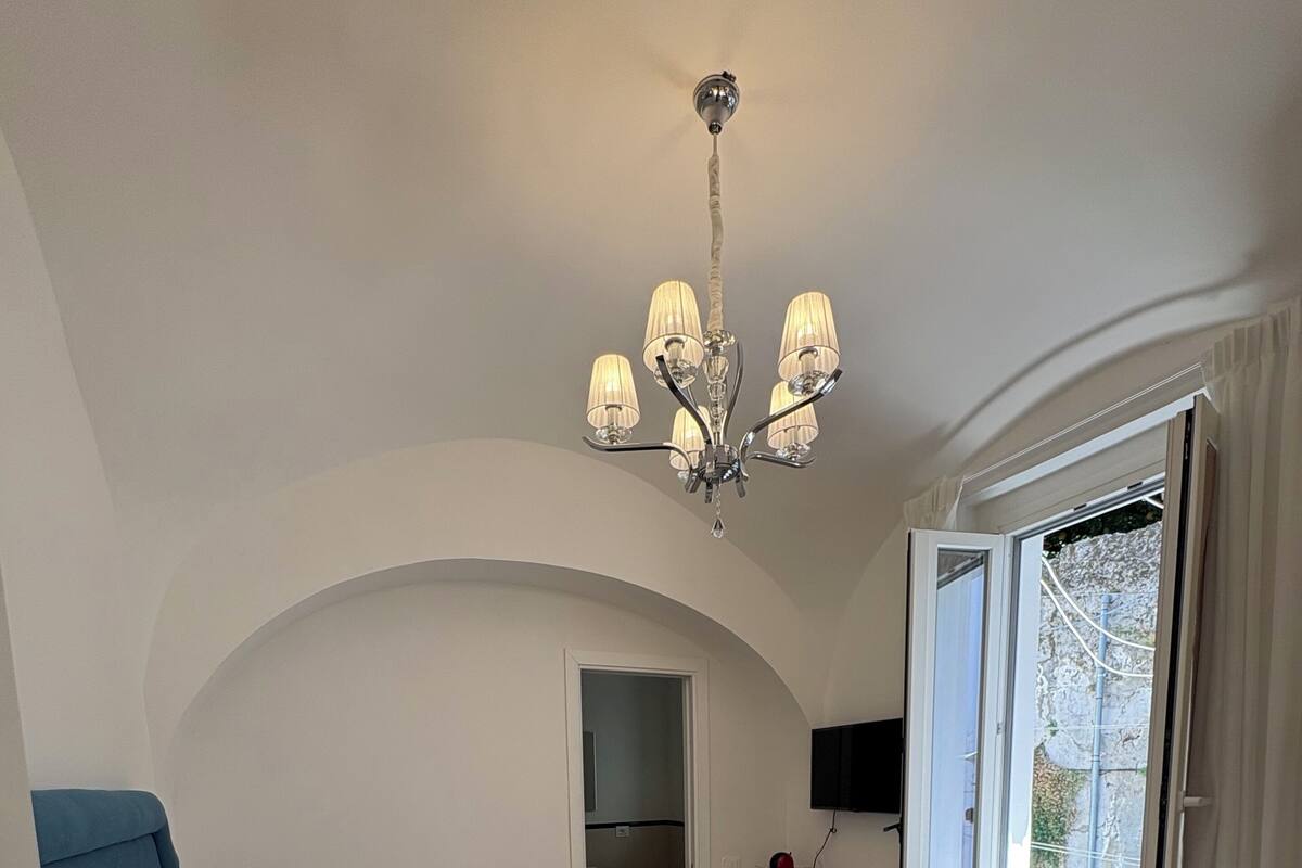 A bedroom with a bed, a desk, a chair, a window, and a chandelier.