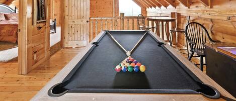 Une table de billard dans une pièce en bois avec un plafond en pente, une table à manger et des chaises.