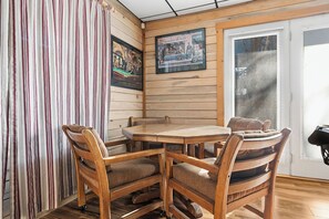 A wooden interior with a dining table and chairs, wooden walls, a window with blinds, and two framed pictures. - Riding The Feathers Of Heaven (GATLINBURG)