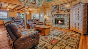 A spacious living room with leather sofas, a fireplace, and a stone wall. - Riding The Feathers Of Heaven (GATLINBURG)