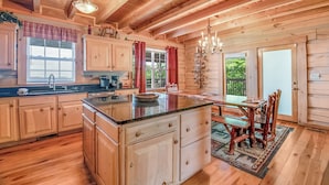 A wooden cabin interior with a kitchen, dining area, and a large window. - Riding The Feathers Of Heaven (GATLINBURG)