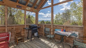 Eine Holzdauerdecke mit Grill, Stühlen und einem Tisch mit Tischdecke.