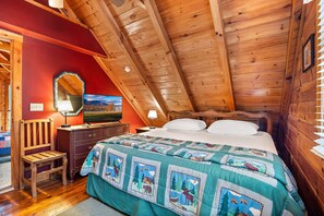 Ein gemütliches Schlafzimmer mit Holzbalkendecke, einem Bett mit Steppdecke, einem Schminktisch, einem Stuhl und einem Spiegel.