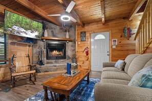 A cozy cabin interior with a stone fireplace, wooden furniture, and a television mounted on the wall. - Claim Your Piece of Sunset Solitude: Family Getaway in the Smoky Mountains (PIGEON FORGE)