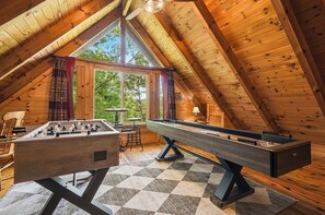 A cozy room with wooden walls and a sloped ceiling, featuring a foosball table and a shuffleboard table. - Claim Your Piece of Sunset Solitude: Family Getaway in the Smoky Mountains (PIGEON FORGE)
