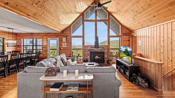 A spacious loft-style room with a high ceiling, large windows, a fireplace, and a cozy seating area. - Views For Days And City Lights (PIGEON FORGE)