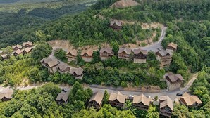 A resort with multiple wooden cabins, winding roads, and dense forested hills. - Views For Days And City Lights (PIGEON FORGE)