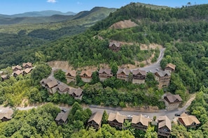 A resort with multiple wooden cabins, winding roads, and dense forested hills. - Views For Days And City Lights (PIGEON FORGE)