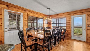 A wooden-paneled dining room with a large table and chairs, a chandelier, and a door with a view of the outdoors. - Views For Days And City Lights (PIGEON FORGE)