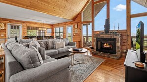 A cozy log cabin interior with a fireplace, a sofa, and a dining area. - Views For Days And City Lights (PIGEON FORGE)