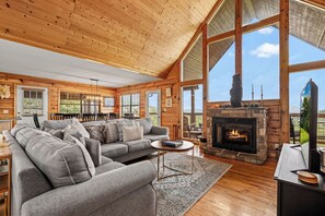 A cozy log cabin interior with a fireplace, a sofa, and a dining area. - Views For Days And City Lights (PIGEON FORGE)
