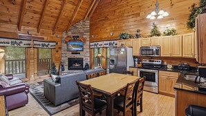 A cabin interior with a fireplace, wooden dining table, kitchen area, and a cozy seating area. - Resort Location*15 minutes to Dollywood*Sleeps 10 (Pigeon Forge)