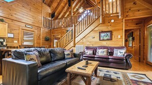 A wooden interior with a staircase, two leather sofas, a coffee table, and a patterned rug. - Resort Location*15 minutes to Dollywood*Sleeps 10 (Pigeon Forge)