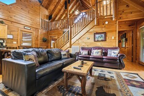 Un intérieur en bois avec un escalier, deux canapés en cuir, une table basse et un tapis à motifs.